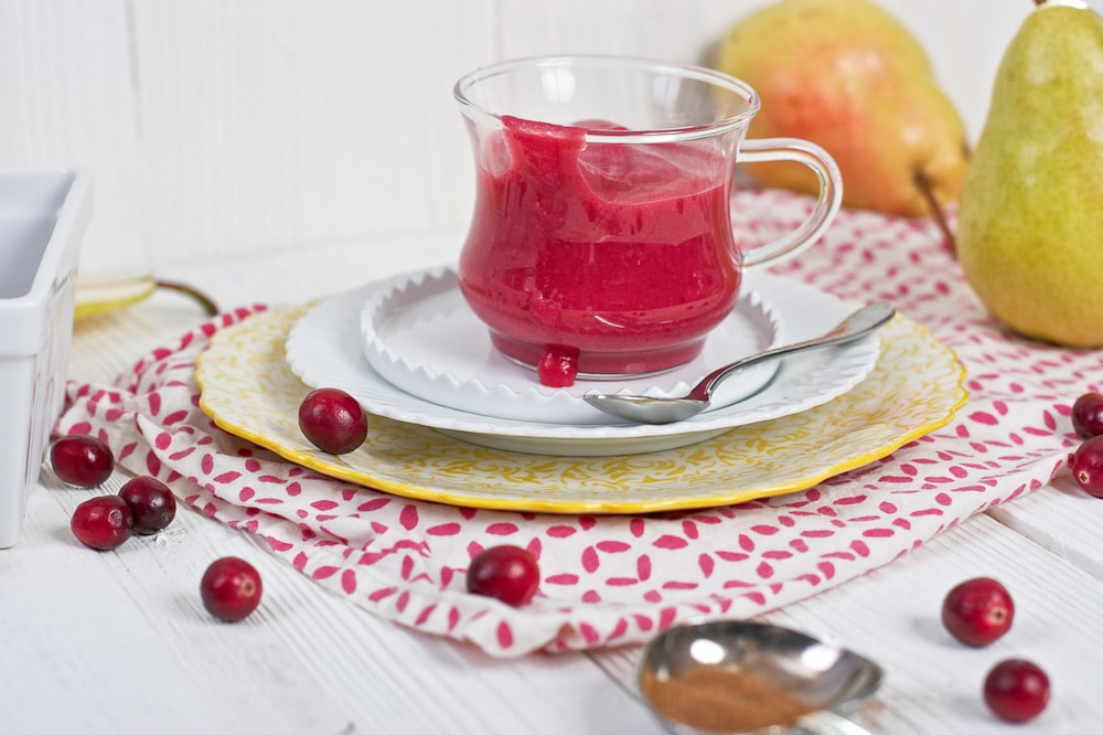 Clear jar filled with a cranberry baby puree sitting on a stack of plate.