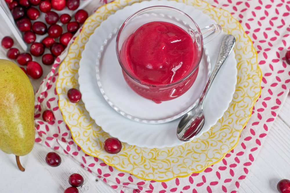 Clear jar filled with a cranberry baby puree sitting on a stack of plate.