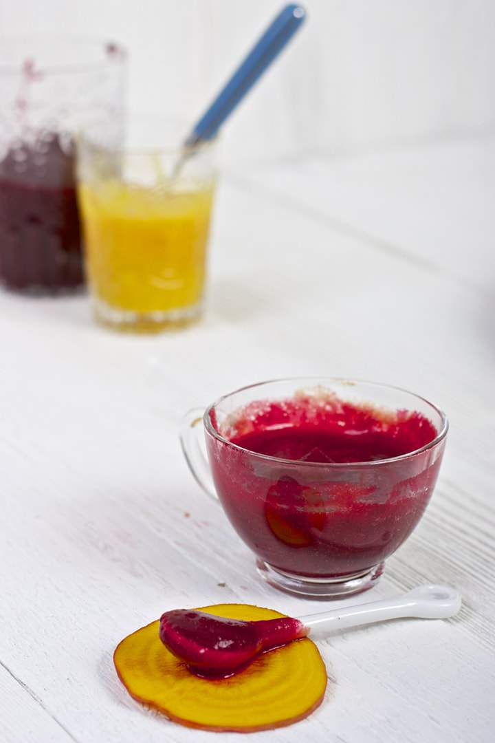 clear jar filled with red beet puree with a spoon sitting in front of it resting on a piece of golden beet.