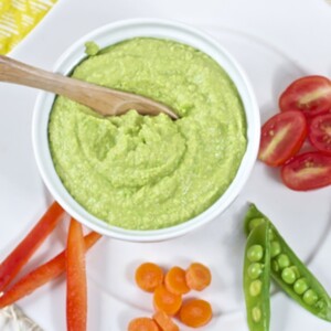 Image is of a small bowl filled with hummus on a plate with chopped veggies.