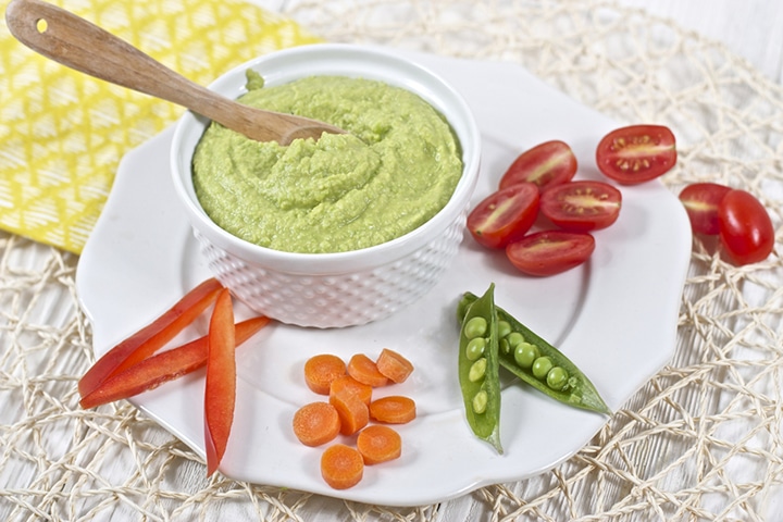 Image is of a small bowl filled with hummus on a plate with chopped veggies.