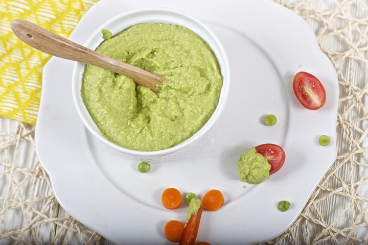 Image is of a small bowl filled with hummus on a plate with chopped veggies.