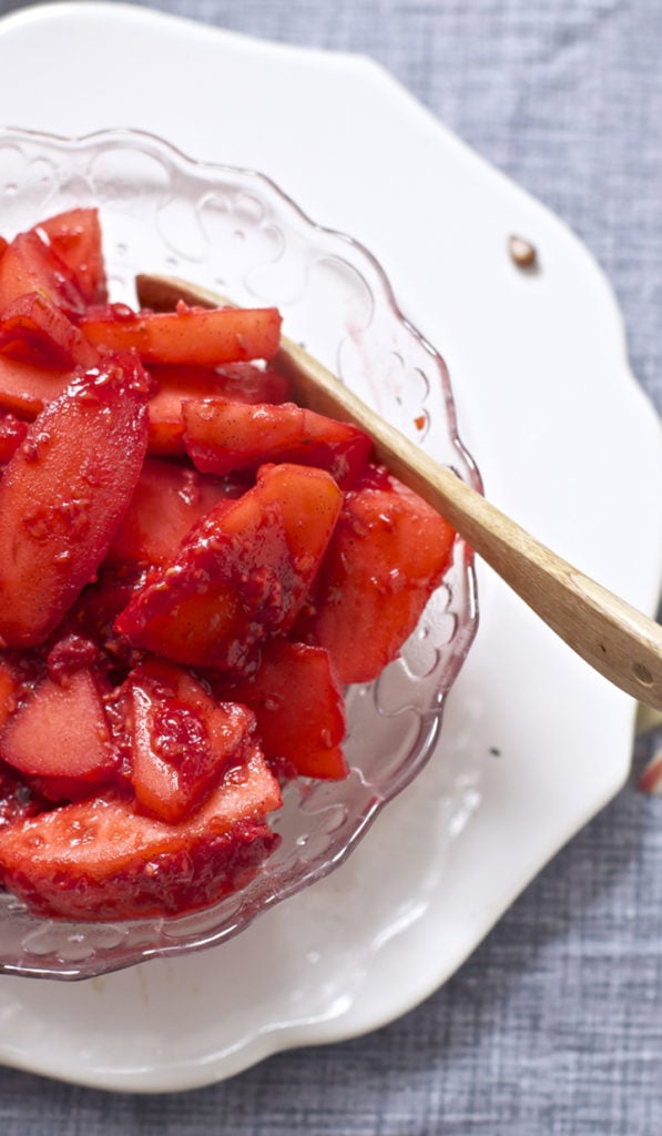 Bowl filled with cooked apples and raspberries with a wooden spoon.