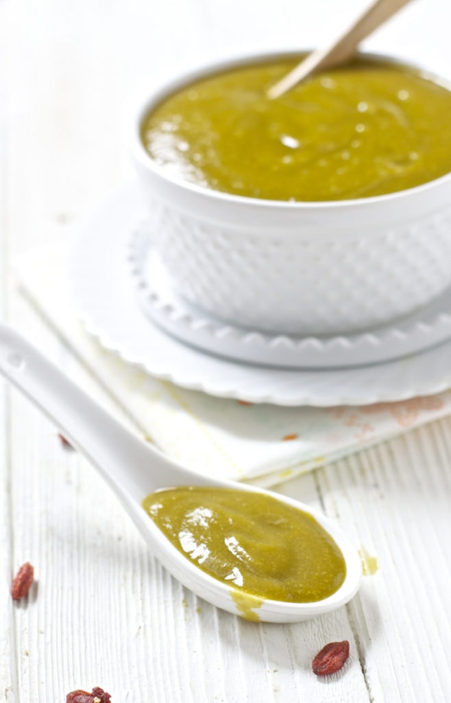 White spoon filled with creamy homemade baby food puree in front of big bowl of puree.