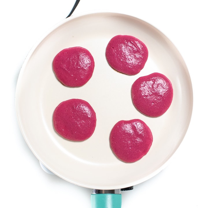 Small white skillet with pink pancakes in small circles cooking on it.