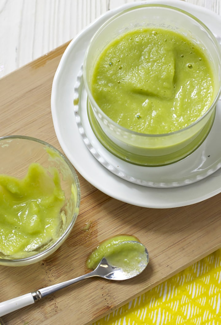 Image is of a glass bowl filled with the homemade puree sitting on a cutting board next to an scrapped empty baby bowl of food.
