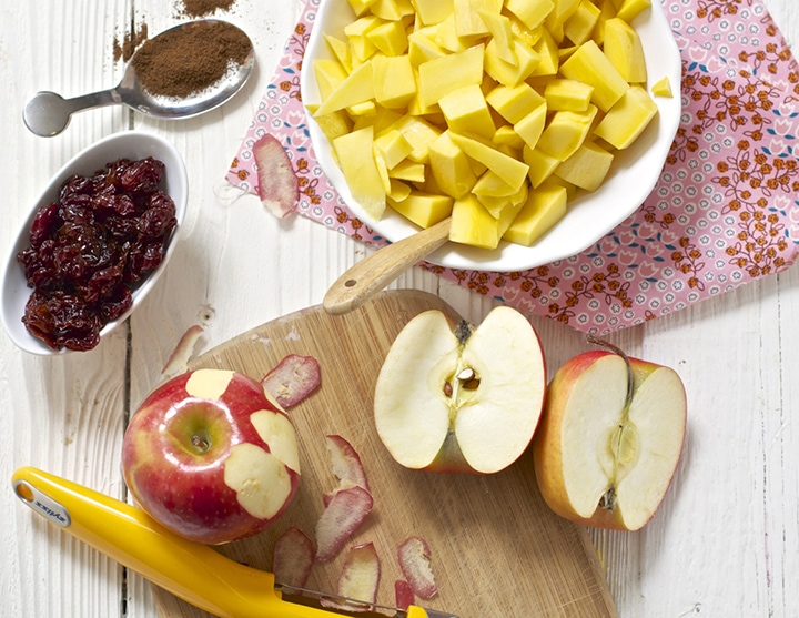 Mango, apples and cherries spread out on a white board.