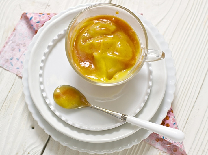 Clear bowl of baby food with spoon resting next to it.
