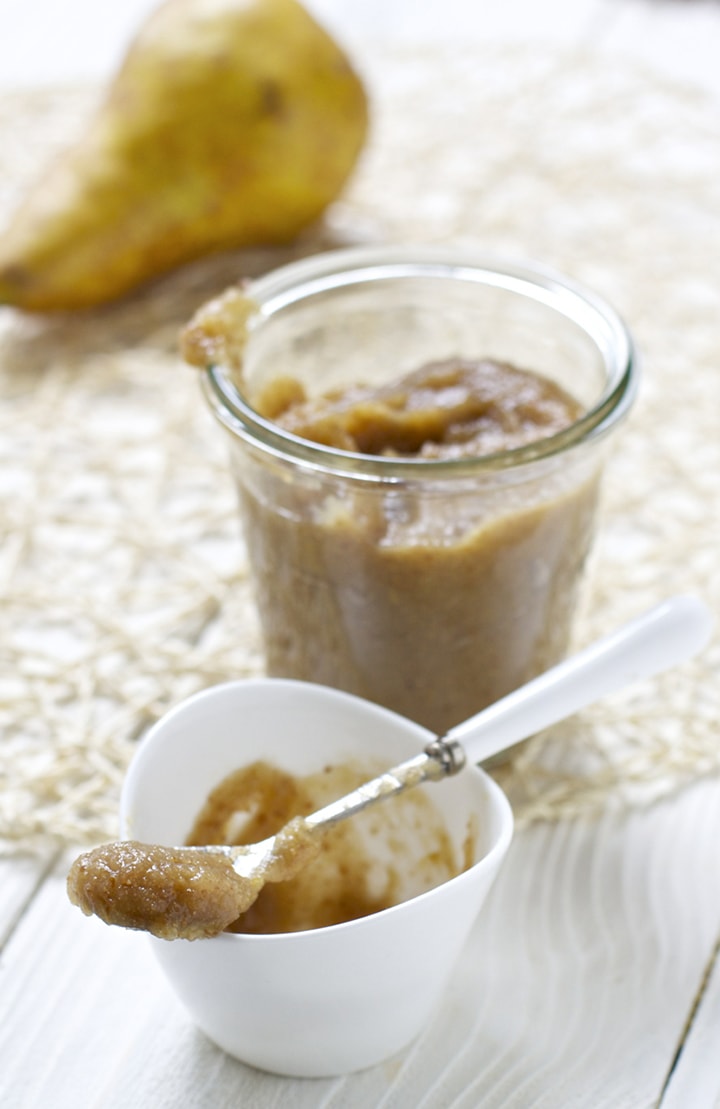 Small white bowl with a baby spoon resting on top filled with baby food with a bigger far behind it filled with puree.
