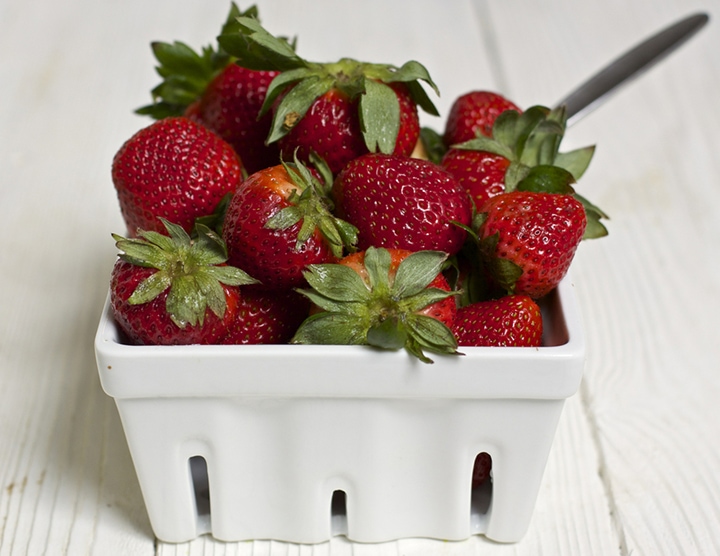White fruit basket with fresh strawberries inside.