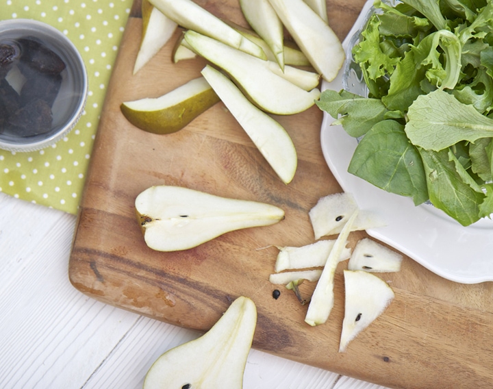 Cut pears on a cutting board with super greens next to it.