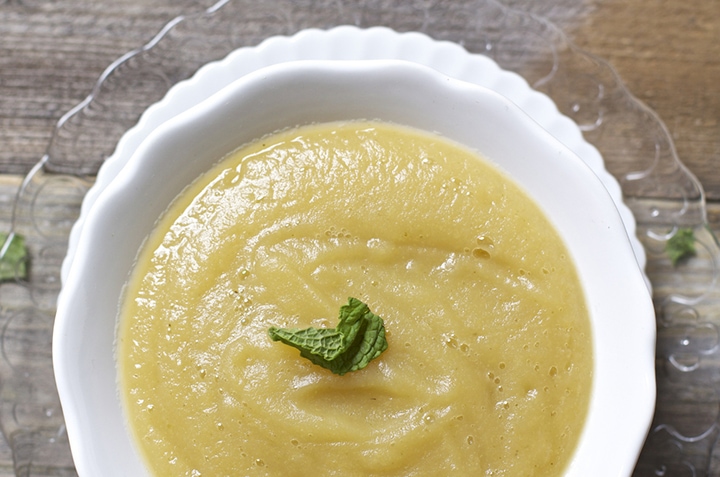 Bowl filled with apple puree with a mint leave on top.