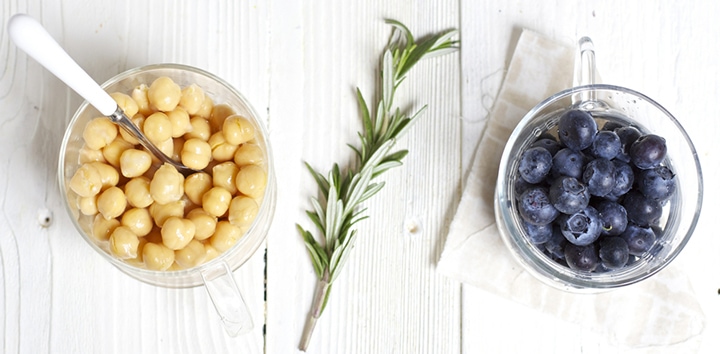 Jars filled with chickpeas and blueberries and sprig of rosemary between them.