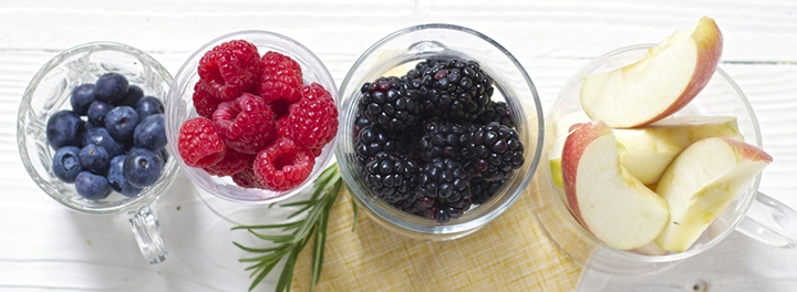 Line of glass bowls filled with berries and sliced apples.