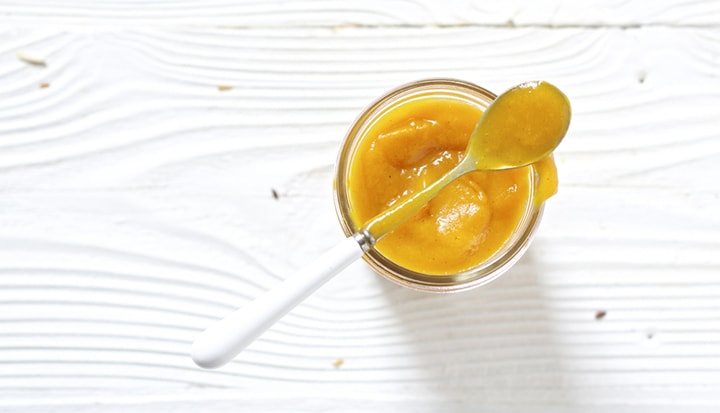 Glass jar filled with a thick homemade baby food puree with a spoon resting on top.