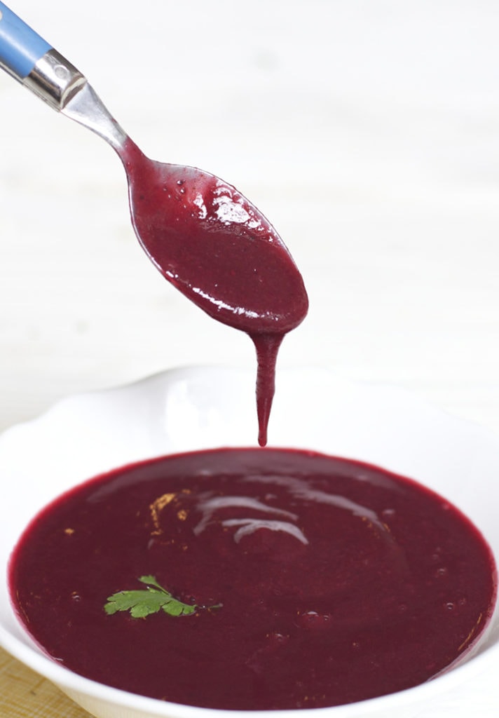 Small white bowl filled with homemade puree with spoon dripping the puree back into the bowl.