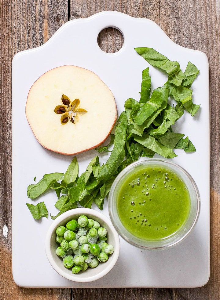 image of a white cutting board with produce scattered on it and a small bowl filled with the baby food puree.