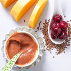 Small white cutting board with ingredients spread around it and a small bowl of baby food puree.