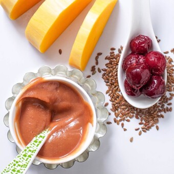 Small white cutting board with ingredients spread around it and a small bowl of baby food puree.
