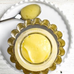 small clear jar sitting on a silver plate and white plate. The jar is filled with acorn squash baby food puree.