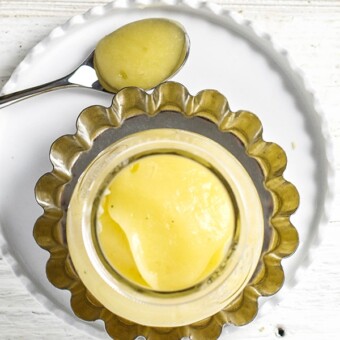 small clear jar sitting on a silver plate and white plate. The jar is filled with acorn squash baby food puree.