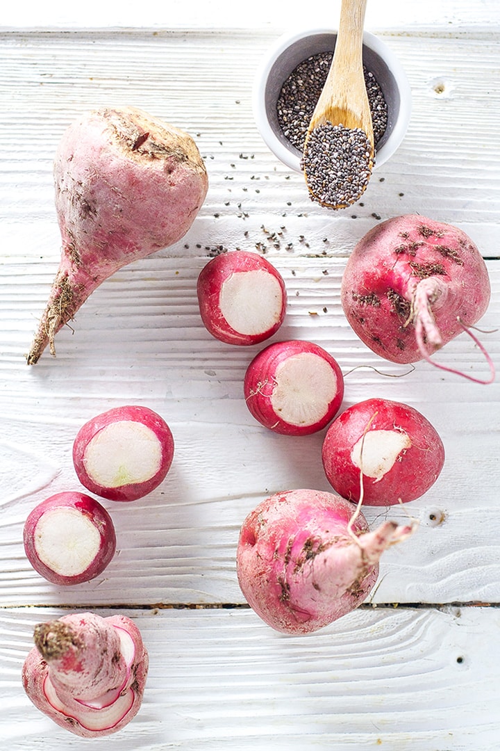 Spread of cut radishes, beets and chia seeds on a white board.