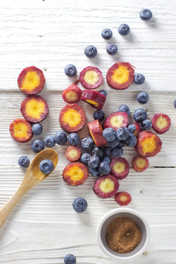 Cut purple carrots and blueberries with a spoon and small bowl of nutmeg.