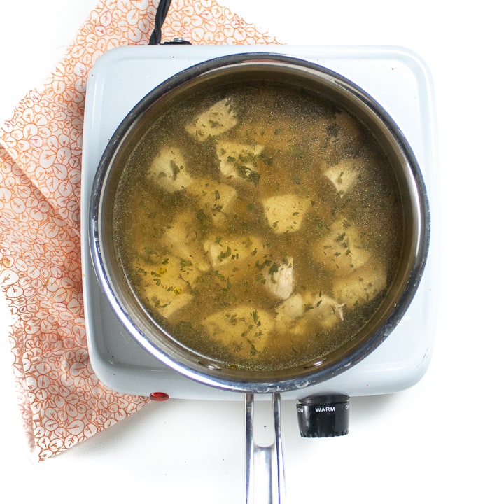 Saucepan full of broth, cooked hicken and parsley.