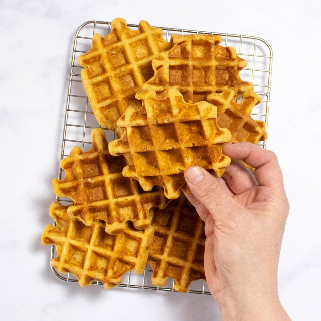 Sweet potato waffles cooling on a wire rack with my hands holding up a waffle to show how fluffy they are.