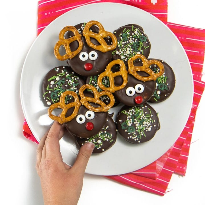 Small kids hands reaching for a reindeer cookie.
