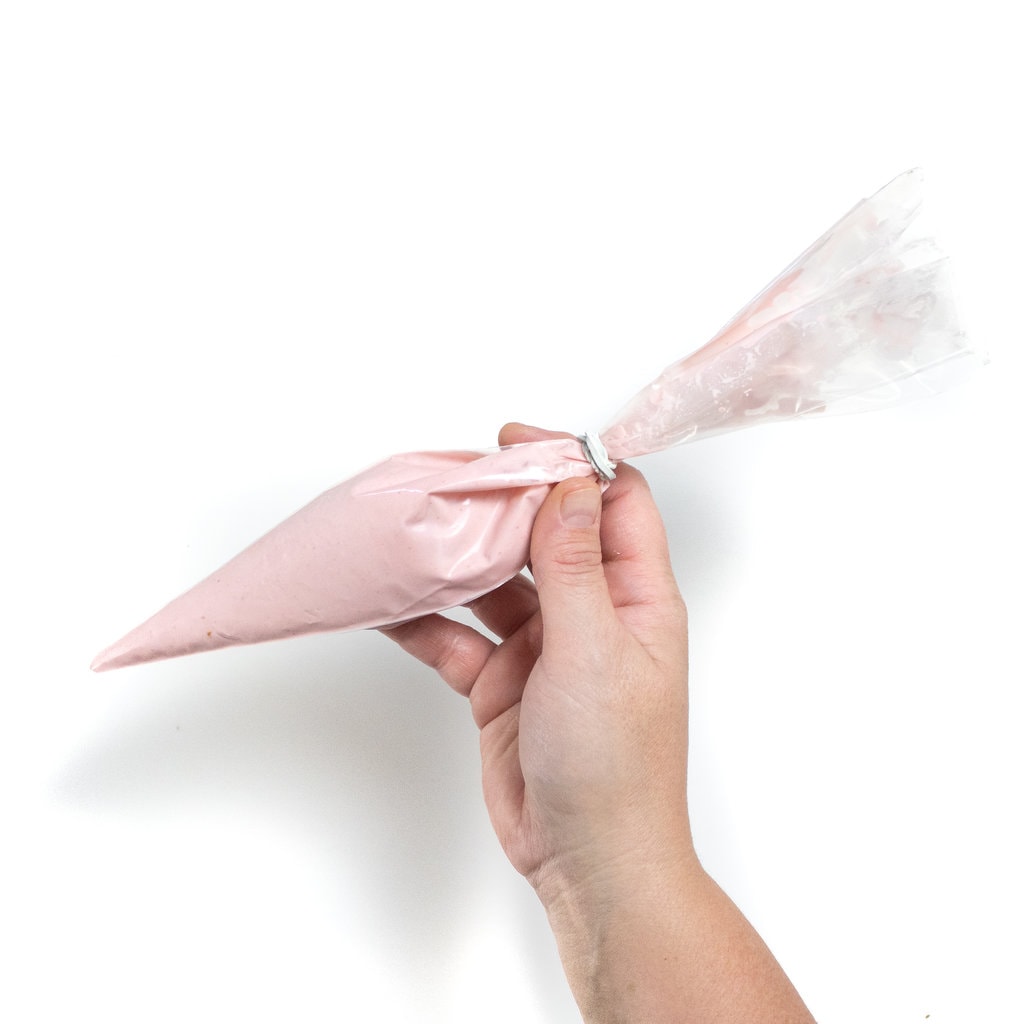 A hand holding a piping bag full of yogurt and baby food purée against a white background ground.