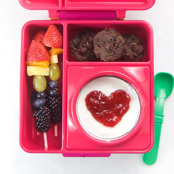Pink school lunch box filled with healthy school lunch ideas - yogurt, rainbow fruit and chocolate muffins