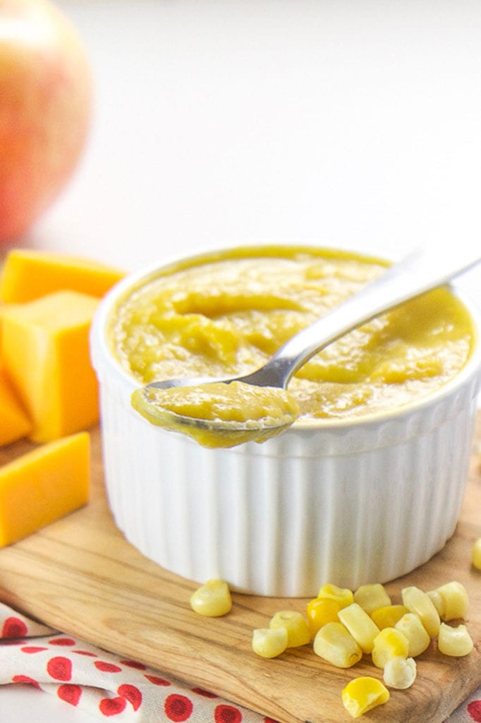 A small white bowl filled with a corn, squash and apple baby food puree.
