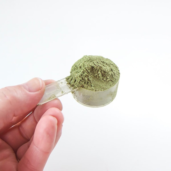 hand holding a scoop of green powder