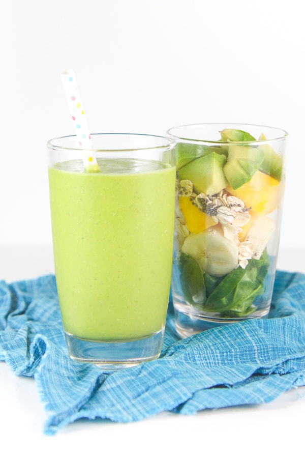 Baby friendly green spinach smoothie in a glass with a separate glass filled with whole smoothie ingredients.