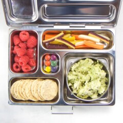 silver planetbox bento box filled with avocado chicken salad, crackers, raspberries, carrots and dye-free candy.