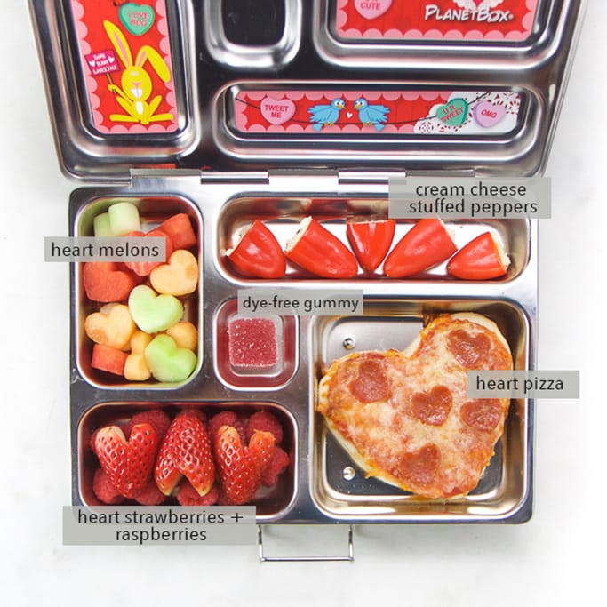 Image is of a school lunch box with valentine themed food inside.
