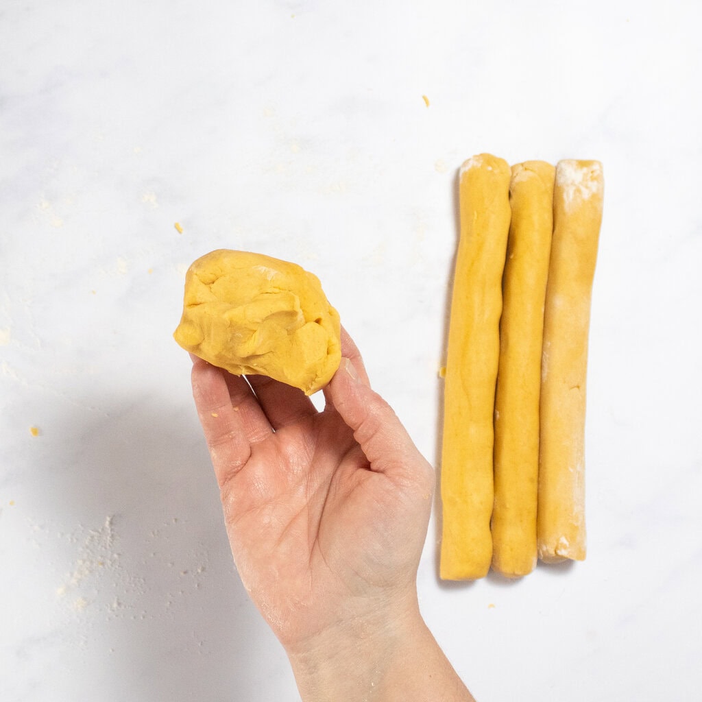 My hand holding up a dough ball of cheese crackers with ropes of the dough on the counter next to my hand.
