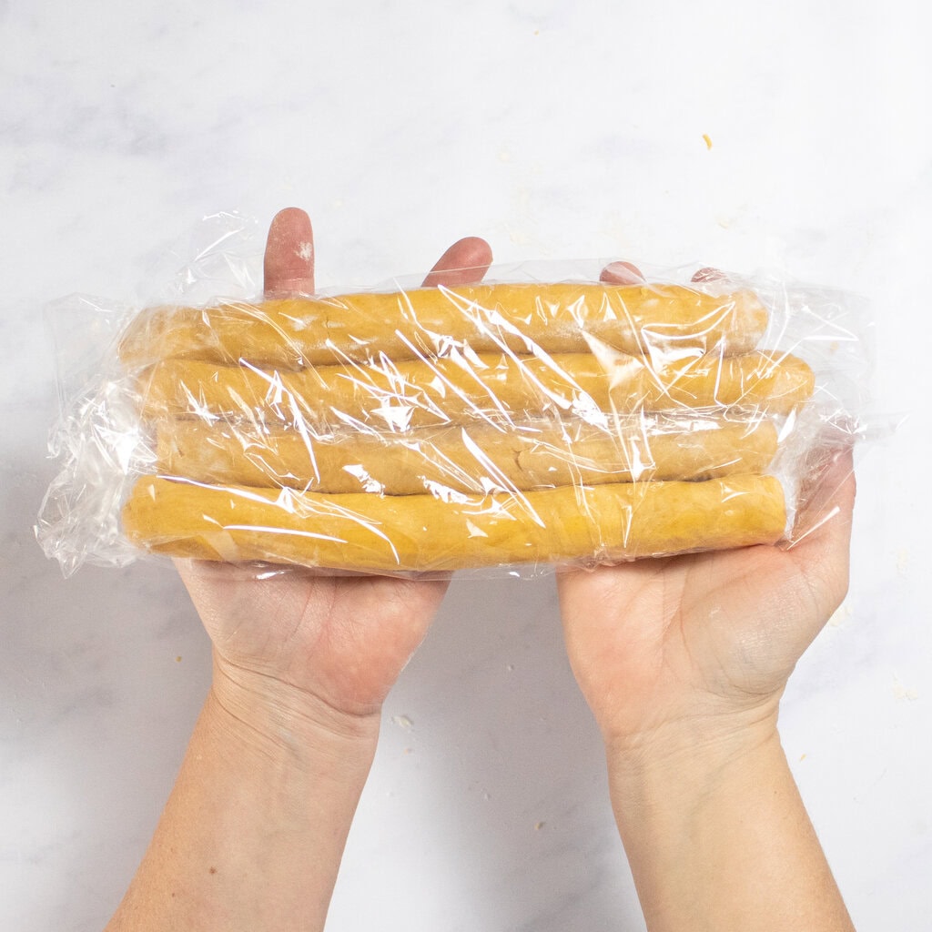 My hands holding four ropes of cheese cracker dough over my white kitchen counter.