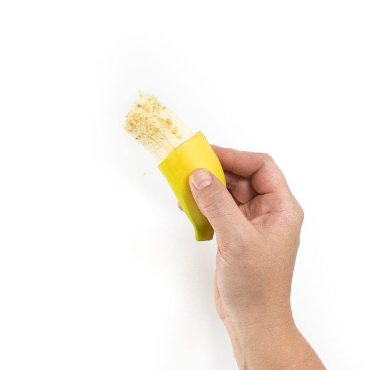 Hand holding a banana wit a sprinkle of finely crushed peanuts on it.