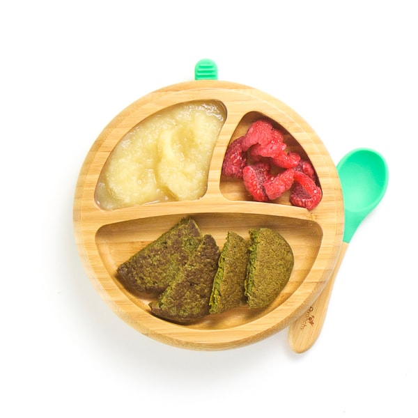 breakfast on wooden plate with 3 sections - spinach pancakes cut in half, applesauce and cut raspberries