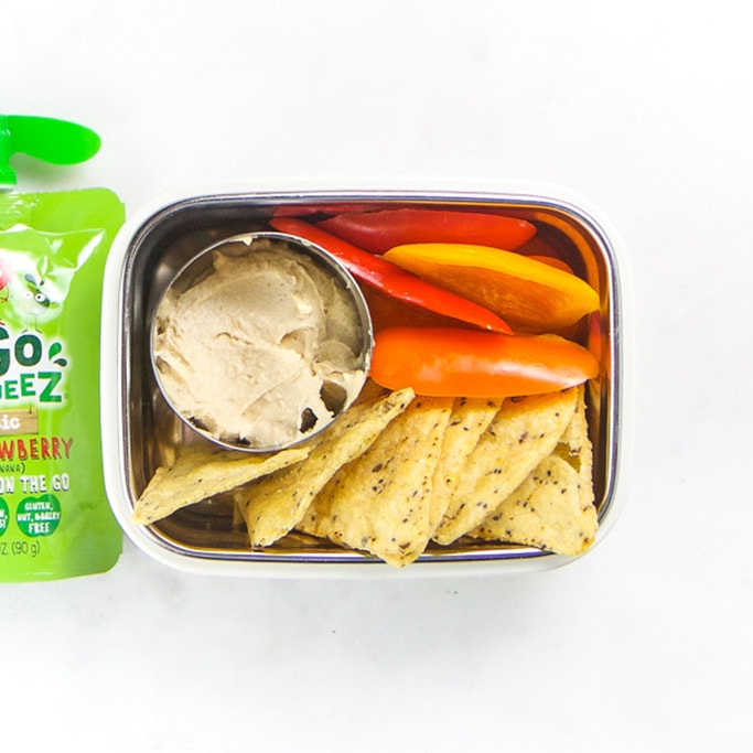 Rectangle kids bento box - small round container with hummus, cut bell peppers, grain chips and an apple pouch sitting off to the side.
