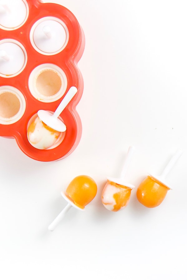 white background with a zoku popsicle mold in the corner and three hidden veggie healthy toddler snack popsicles coming out of it.