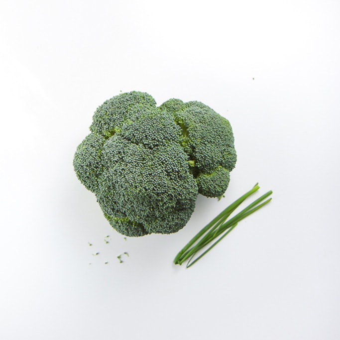 a head of broccoli and a few stalks of chives sitting on a white background