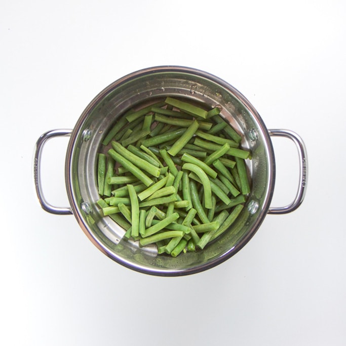 silver steamer sitting on a white background filled with chunks of steamed green beans