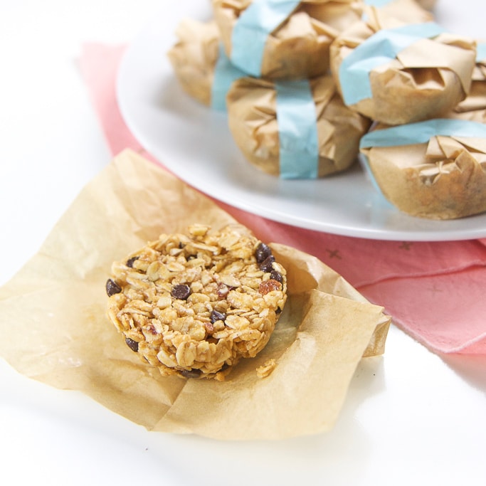 side angle shot of an opened granola bar with the beige liner underneath it. The granola bar is sitting in front of plate of wrapped granola bars
