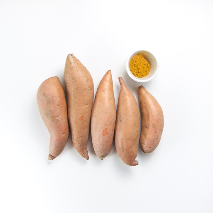 5 small sweet potatoes lined up in a row with a small bowl filled with a mild curry spice inside.