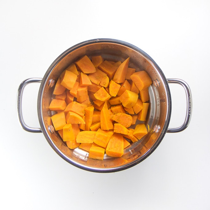 silver steamer basket filled sitting on a white background filled with steamed sweet potato chunks
