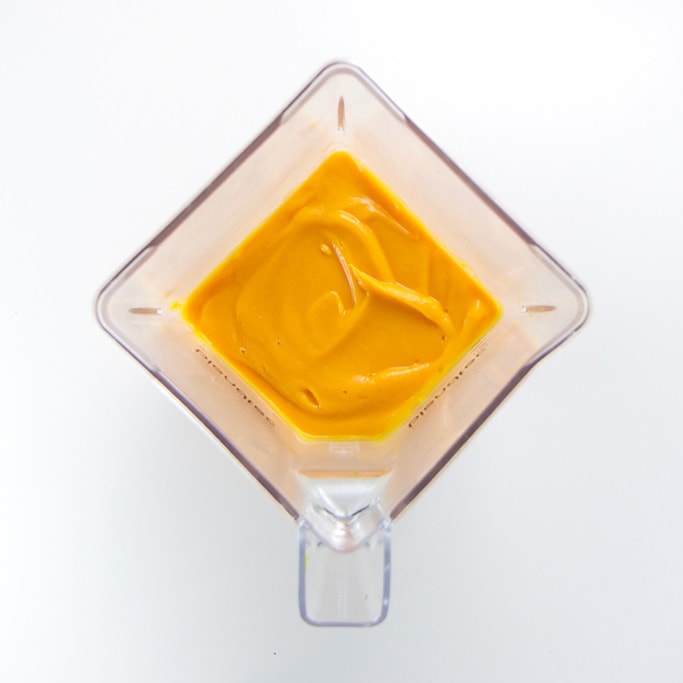 blender sitting on a white backdrop filled with a smooth sweet potato curry baby food puree