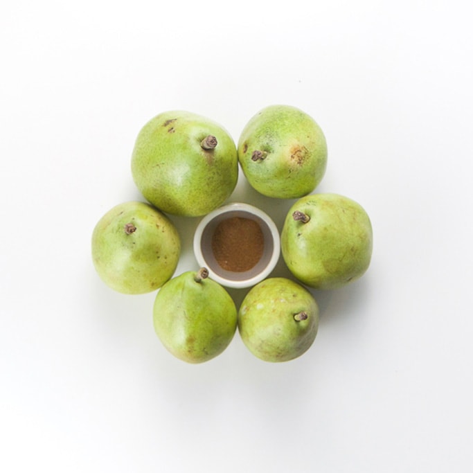 6 green pears on a white background in a circle. Inside the circle is a small bowl with ground clove inside.